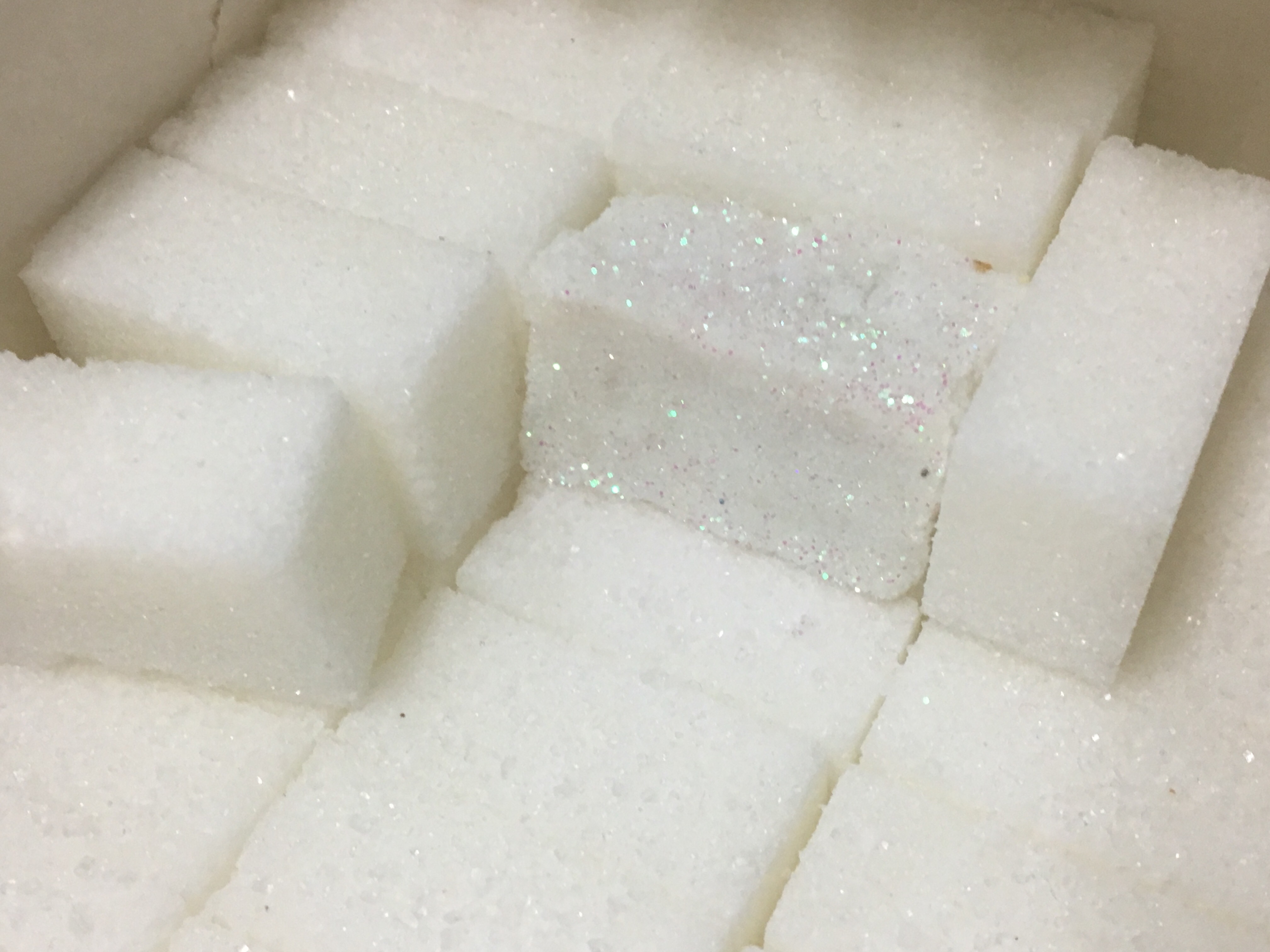 Gros plan sur la boîtee à sucres. Un des sucres est fait avec des paillettes blanches aux reflets nacrés rose et bleu.